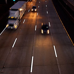 An overhead shot of cars and a semi-truck driving on a highway at night, with brightly illuminated pavement markings.