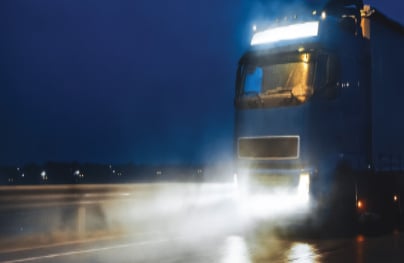 Semi truck with cargo trailer driving on wet road at night.