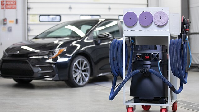 3M sanding and dust‑extraction cart in a shop with a car in the background
