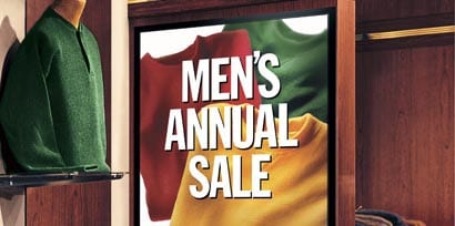A zoom in view of a promotional sign for a men's annual sale with a red, green, and yellow shirt on it printed using 3M printable films.
