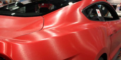 A red sports car has a red vehicle wrap with a textured overlaminate.
