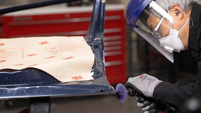 Worker using a 3M abrasive disc on metal while wearing safety gear.

