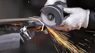 A gloved hand operating a rotary industrial grinding wheel on metal, creating bright sparks during grinding
