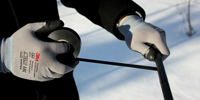 worker wrapping electrical cable in electrical tape in winter
