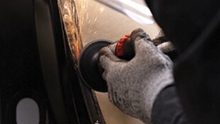 A gloved hand using a handheld abrasive tool on a metal surface, generating sparks
